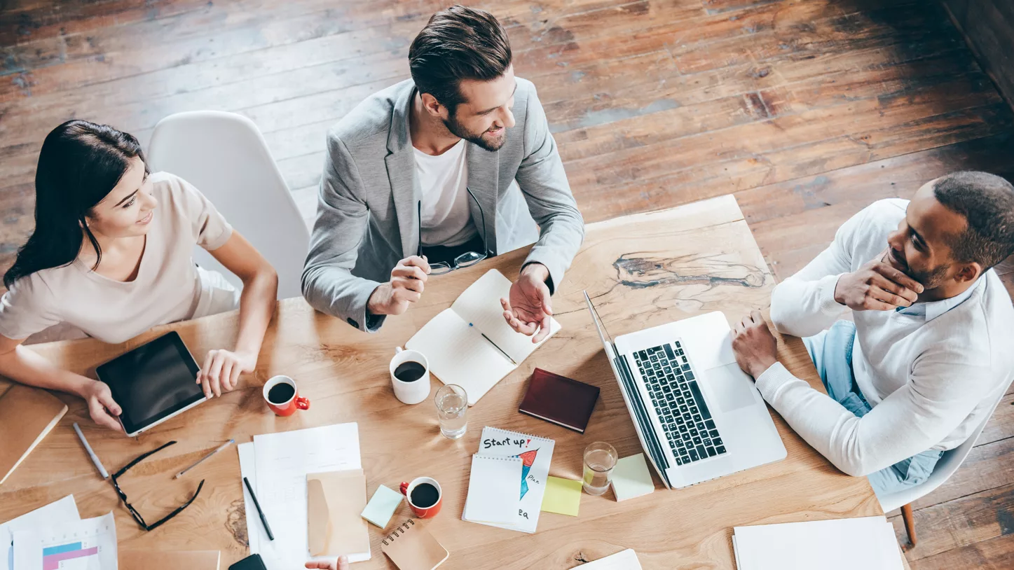 A team collaborates around a wooden table. They listen to each other and share their points of view. 