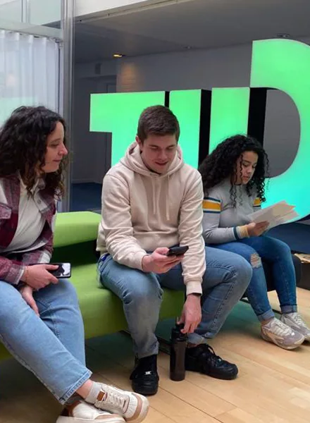 Jeunes collaborateurs assis dans un espace moderne, utilisant leur smartphone et échangeant des documents, illustrant un onboarding stratégique centré sur l’expérience.